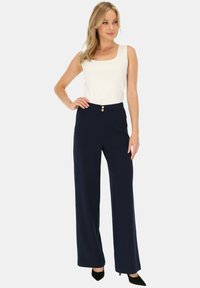 Granatowe szerokie spodnie wykonane z tkaniny, z dopasowanym fasonem w talii i dwoma złotymi guzikami. Połączone z białym topem bez rękawów i czarnymi obcasami.