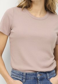 Jasnoróżowa, prążkowana koszulka z krótkim rękawem, okrągłym dekoltem i dopasowanym krojem, zestawiona z dżinsami z guzikiem.