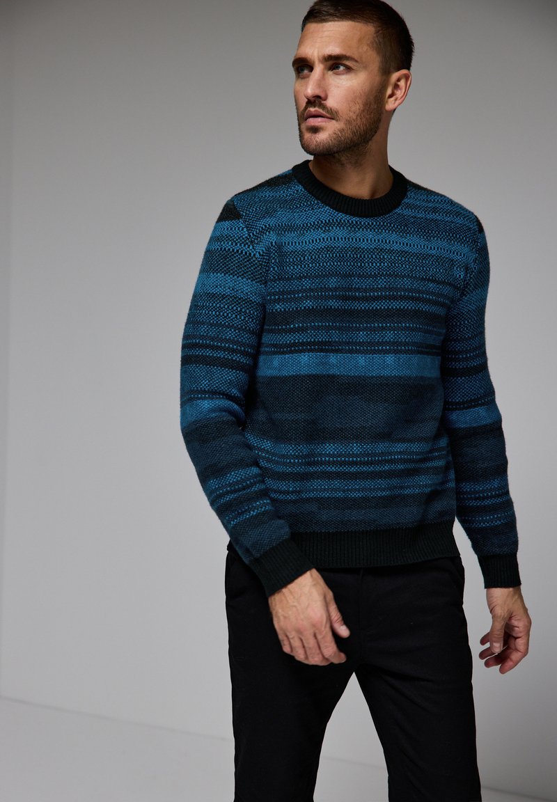 Jersey de punto en azul oscuro con rayas horizontales en diferentes tonalidades de azul y negro; cuenta con un cuello redondo y puños de canalé.