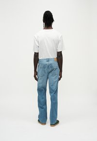 Ανοιχτό γκρι κοντομάνικο μπλουζάκι, σε συνδυασμό με μπλε τζιν παντελόνι. Το τζιν έχει ίσιο κόψιμο, αποχρωματισμένη υφή και ένθετο λογότυπο στο πίσω μέρος.