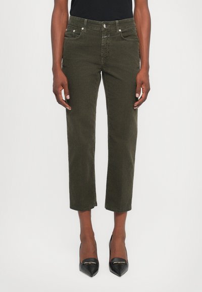 Pantaloni in velluto a coste verde oliva, taglio cropped, con tasche frontali e chiusura a bottone, abbinati a décolleté nere a punta per creare contrasto.