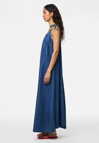 Traper haljina maksi dužine s opuštenim krojem, vezanjem na ramenima i tamnoplavom bojom. Lagani materijal s čvrstim uzorkom, doseže pri kraju do gležnjeva.