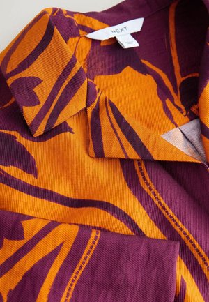 Lühikeste varrukatega särk oranžikas ja lilla velvetkangas, millel on julged lillemustrit ja sälguv krae. Siseosas on nähtav brändisilt.