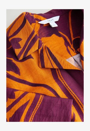 Lühikeste varrukatega särk oranžikas ja lilla velvetkangas, millel on julged lillemustrit ja sälguv krae. Siseosas on nähtav brändisilt.