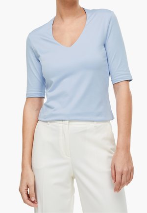 Lyseblå top med korte ærmer og dyb V-hals, glat stof og en afslappet pasform, kombineret med hvide bukser.