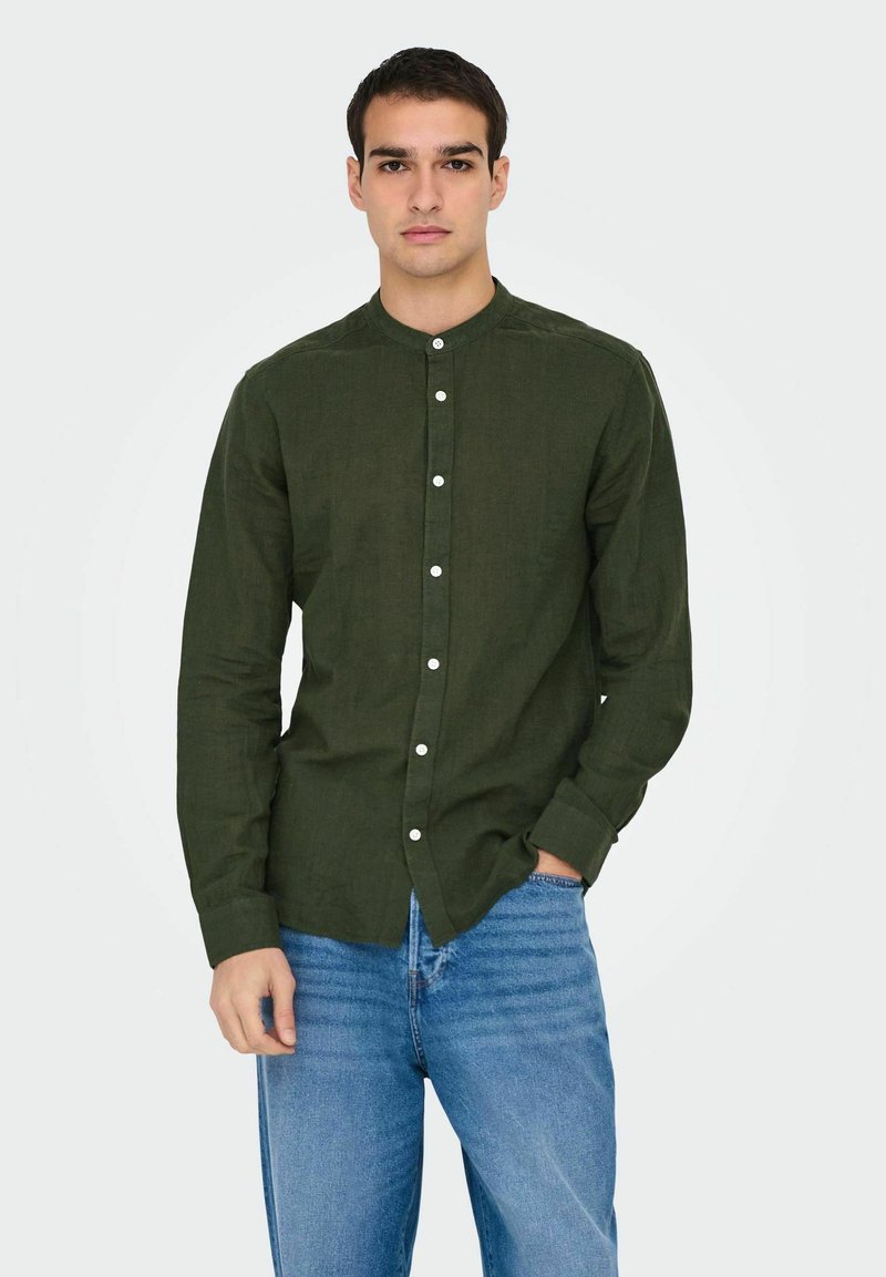 Chemise à manches longues verte, boutonnée, en tissu léger avec un col montant et des boutons blancs, associée à un jean bleu.