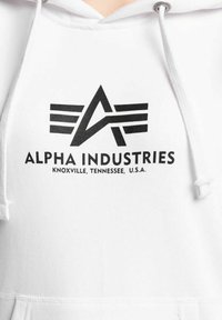 Vit hoodie med en svart grafisk logotyp där "ALPHA INDUSTRIES" står tryckt tillsammans med "KNOXVILLE, TENNESSEE, U.S.A." nedanför. Hoodie med snörning.