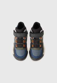 Scarpe da ginnastica nere e grigie con accenti blu e verdi, dotate di cinturini regolabili, suole testurizzate e dettagli riflettenti.