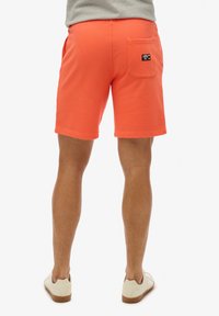 Pantaloni corti corallo vivace con una tasca posteriore e un'etichetta. Realizzati in cotone, presentano una texture liscia e una cintura elastica.
