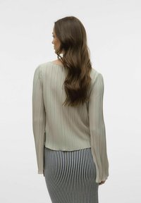 Lys grønn plissébluse med lange ermer, buet kant, myk tekstur, kombinert med et stripete skjørt for et lagdelt utseende.