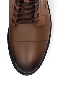 Brązowy skórzany but z zaokrąglonym czubkiem, z ciemnymi sznurówkami, gładką fakturą i przeszytym szwem wokół podeszwy. Prosty, funkcjonalny design.