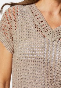 Beige gehaakte top met een v-hals, korte mouwen en een open weefpatroon. Geweven steekdetails overal.