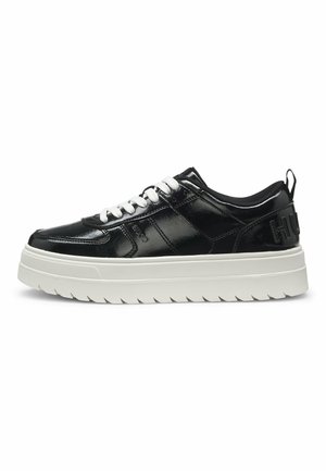 Schwarzer Sneaker in niedriger Ausführung mit glänzendem Finish, weißer dicker Sohle, weißen Schnürsenkeln und Markenname an der Seite und Fersenlasche geprägt.