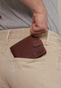 Hnědá kožená peněženka částečně umístěná v světlé zadní kapse. Disponuje prošívaným okrajem a zacvakávacím uzávěrem.