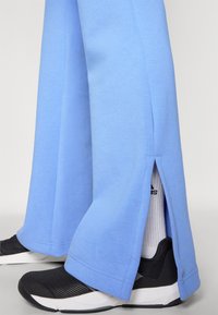 Svijetloplave trenirke širokog kroja, s bočnim prorezima, u kombinaciji s crnim sportskim cipelama i bijelim čarapama.