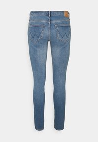 Jeans de denim azul ajustados con un acabado desgastado, que cuentan con dos bolsillos traseros con un patrón de costura diagonal y una etiqueta de marca de piel marrón en la cintura.