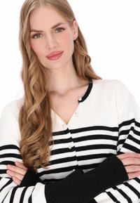 Cárdigan a rayas blancas y negras con textura acanalada, con botones de perla y mangas largas negras, diseñado con escote en V.