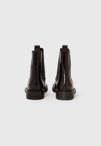 Botines de cuero marrón con un acabado brillante, paneles laterales elásticos, una cinta en la parte trasera y una suela plana y resistente.