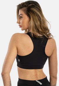 Svart sports-bh med brede skulderstropper, tettsittende design, glatt tekstur og en liten logo detalj på baksiden.