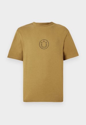 Korte mouwen mosterdkleurig katoenen t-shirt met een ronde halslijn. Heeft een eenvoudig zwart smiley face logo in het midden. Soepele textuur.