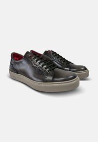 Zapatillas de piel en gris oscuro con cordones verdes, que presentan detalles de brogue, una suela de goma beige y un forro interior rojo.