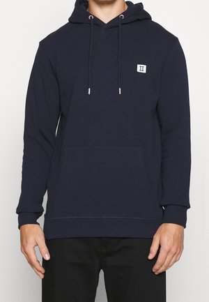 Marineblauer Kapuzenpullover mit Fronttasche, Kordelzug an der Kapuze und kleinem rechteckigem Logopatch auf der linken Brust.