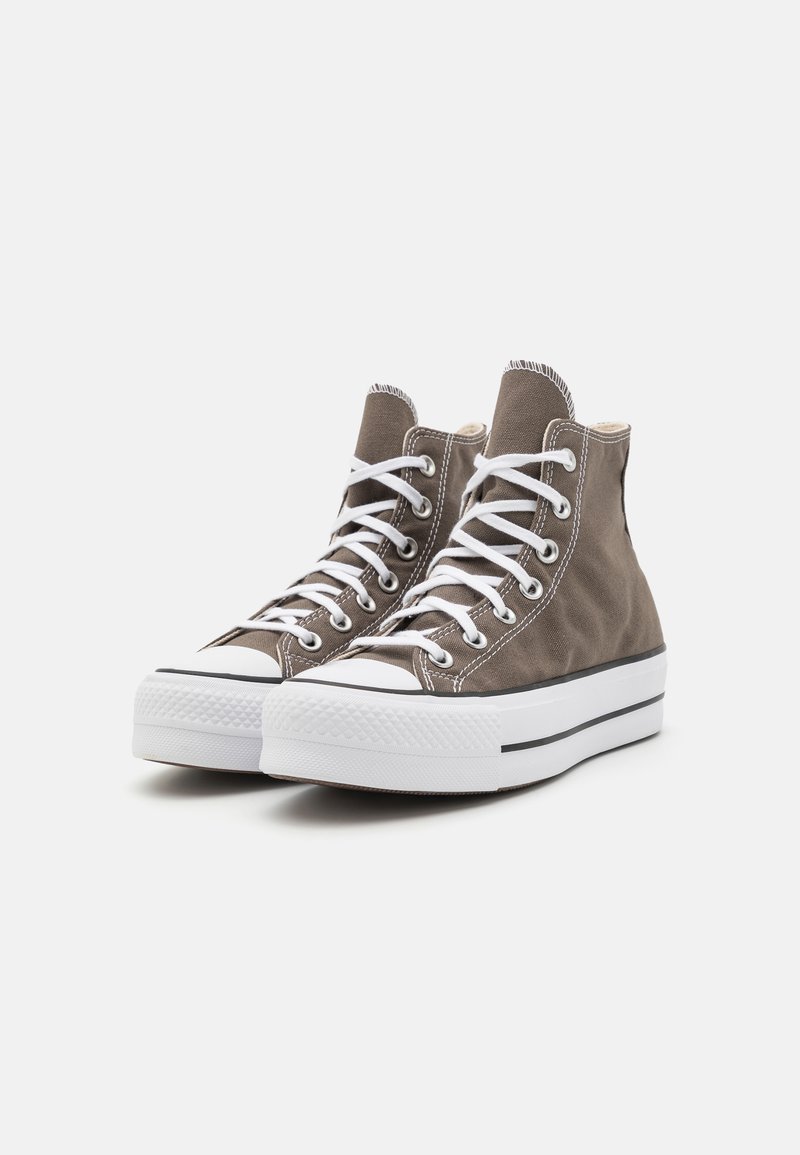 Baskets montantes en toile marron avec semelles en caoutchouc blanc, dotées de lacets blancs, d'accents noirs et d'un capuchon de toe texturé.