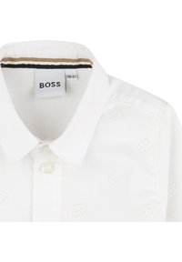 White collared shirt with subtle embossed pattern. Features a button-down placket and a label reading "BOSS." Soft fabric texture.