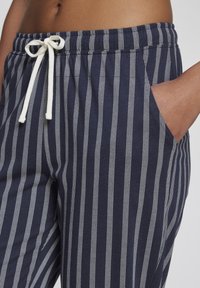 Navy sweatpants with white vertical stripes, featuring an elastic waistband, adjustable drawstring, and side pockets. Soft fabric texture.