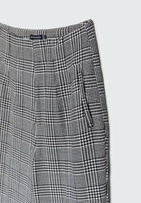 Zwart-wit geblokte broek met een gestructureerde stof, een gestileerde vorm en zijzakken. Het patroon bevat houndstooth accenten.