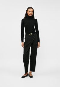 Μαύρο πουλόβερ με φίμωτρο, ψηλόμεσο μαύρο παντελόνι με πιέτες, μαύρη ζώνη με χρυσό πόρπη και μαύρες μυτερές γόβες.