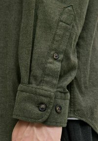Olivengrünes Flanellhemd mit Ärmeln, das zwei schwarze Knöpfe, eine spitze Manschette und einen strukturierten, gewebten Stoff mit einer definierten Nahtlinie trägt.