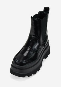 Bottines en cuir noir avec un bout arrondi, des panneaux élastiques sur les côtés et une semelle en caoutchouc épaisse. Présente une sangle à l'avant pour le détail.