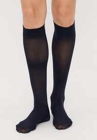 Meias de nádegas até ao joelho em azul-marinho, feitas de um tecido transparente, com uma textura suave e faixas elásticas na parte superior para um ajuste seguro. Os dedos dos pés estão descobertos.