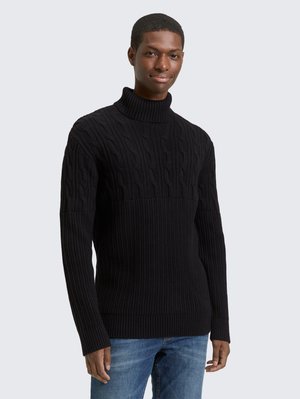 Black cable-knit turtleneck sweater featuring ribbed texture, long sleeves, and a fitted design, paired with blue denim jeans.