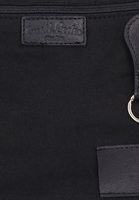 Schwarze Stofftasche mit einem eingenähten Lederetikett mit der Aufschrift "Bussiti Leder Studio" nahe dem oberen Reißverschluss und einem Lederband mit einem Metallring auf der rechten Seite.