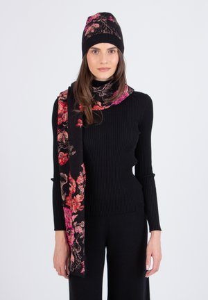 Maglia nera a maniche lunghe con righe, abbinata a una sciarpa nera con motivo floreale e un berretto coordinato con accenti rosa e rossi. Materiali morbidi e texture.