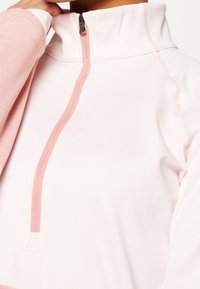 Světle růžový pulovr s vysokým límcem, čtvrtzipem, měkkou texturou látky a kontrastními raglánovými rukávy v hlubší růžové barvě.