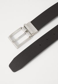 Ceinture en cuir noir avec une boucle en métal argenté. La boucle présente un design rectangulaire simple et des trous réglables le long de la sangle.