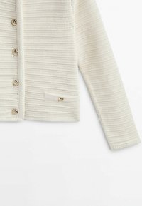 Witte gebreide cardigan met een textuurpatroon, gouden knopen en een zijzak met een gouden accent. Lange mouwen ronden het ontwerp af.