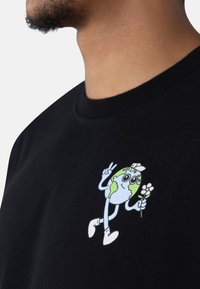 Black cotton T-shirt with a cartoon Earth design featuring green and blue, holding a flower, and making a peace sign.