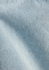 Ljust blå denimtyg med en fin twill väv, som visar en mjuk textur och subtila blekningsmönster. Närbilden framhäver detaljerad sömnad.
