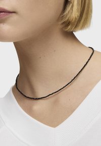 Collana nera di perline realizzata con piccole perle rotonde, indossata a stretto contatto con il collo. Caratterizzata da un design delicato e minimalista.
