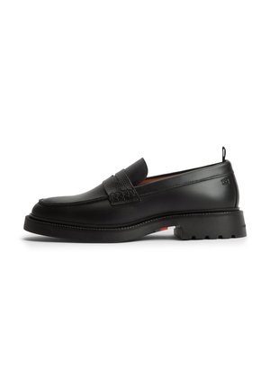 Mocassino nero in pelle con suola spessa, punta arrotondata e dettaglio con fascia sulla parte superiore, mostrato in vista laterale su sfondo bianco.