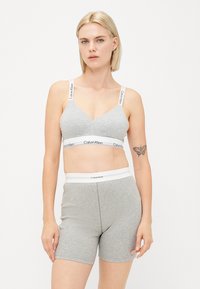 Gray bralette and shorts set made of soft fabric. Bralette features a V-neck and logo-printed straps; shorts have a logo waistband.
