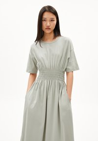 Light green cotton dress with a round neckline, short sleeves, smocked waist, and side pockets, featuring a loose, flowing fit.
