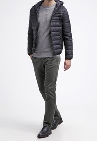 Pánská černá prošívaná bunda s kapucí, šedá mikina a olivově zelené kalhoty, doplněné hnědými koženými botami.