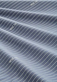 Lichtblauwe stof met witte horizontale strepen, met een gladde textuur en subtiele glans, met een bedrukt merklogo in één hoek.