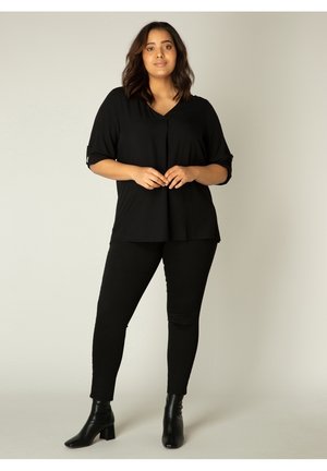 Zwarte top met korte mouwen en V-hals, met knoopdetails, gecombineerd met zwarte skinny jeans en zwarte enkellaarsjes met blokhak.