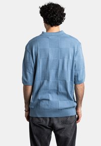 Polo de punto azul claro con un patrón de cuadros texturizado, mangas cortas y puños acanalados. Corte relajado, estilo casual.